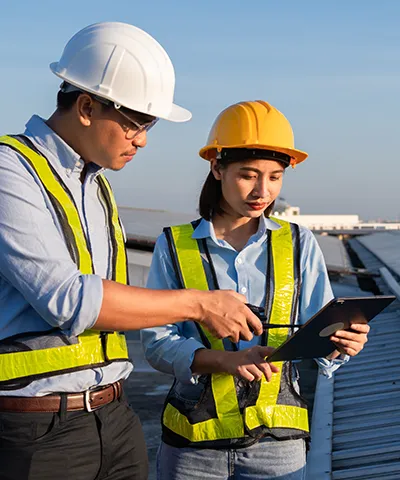 Two construction workers in hard hats reviewing information on a tablet outdoors