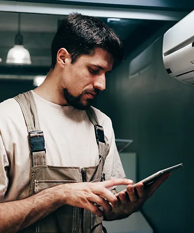 Technician in overalls using a tablet near wall-mounted equipment