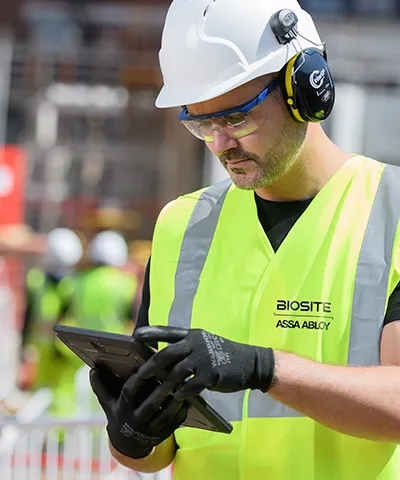 Worker wearing ear protection and gloves using a tablet on a construction site