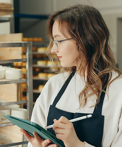 Bakery worker with glasses using a tablet and stylus near shelving racks