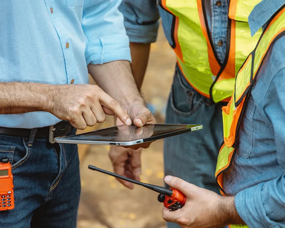 Two workers in safety vests reviewing information on a tablet at a job site