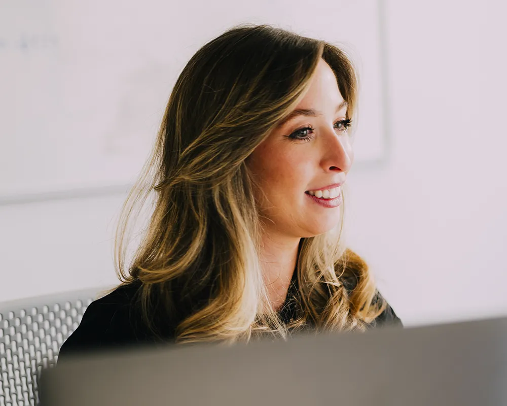 Smiling woman with long hair looking at a computer in a bright office setting