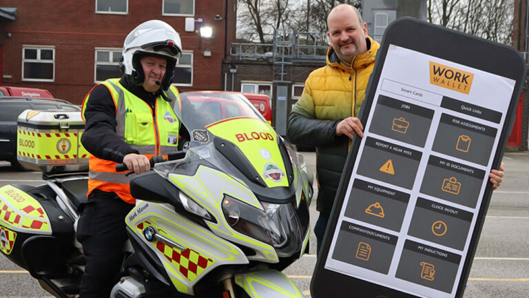 A blood bike rider poses with a man holding a large Work Wallet display board