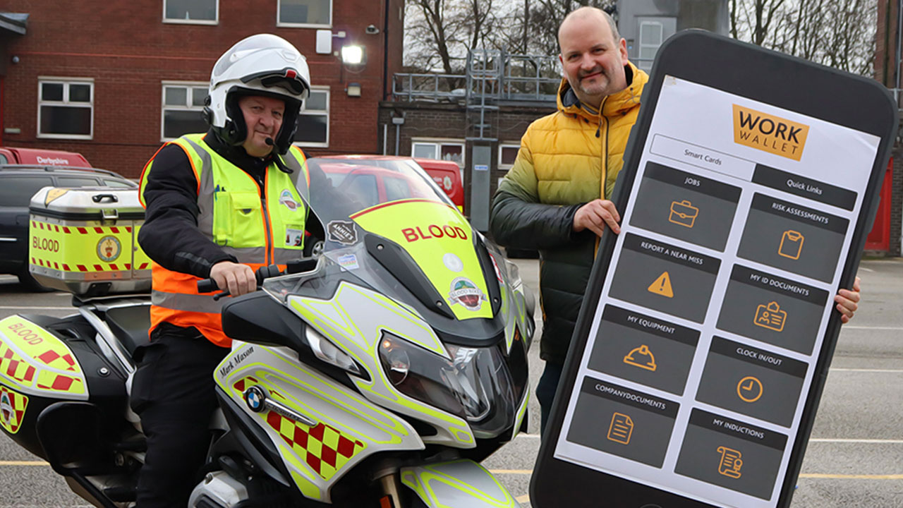 A blood bike rider poses with a man holding a large Work Wallet display board