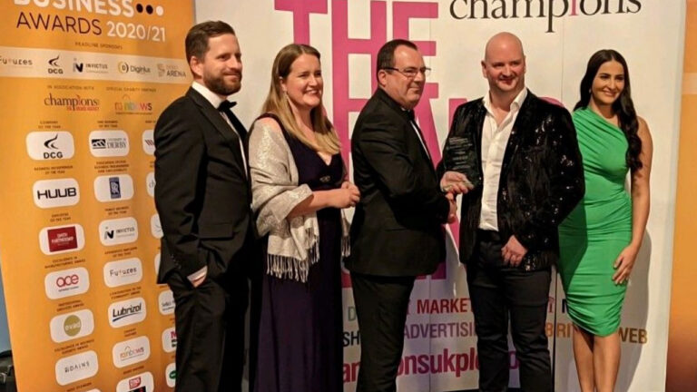 Group of people posing at a business awards ceremony with trophies and banners