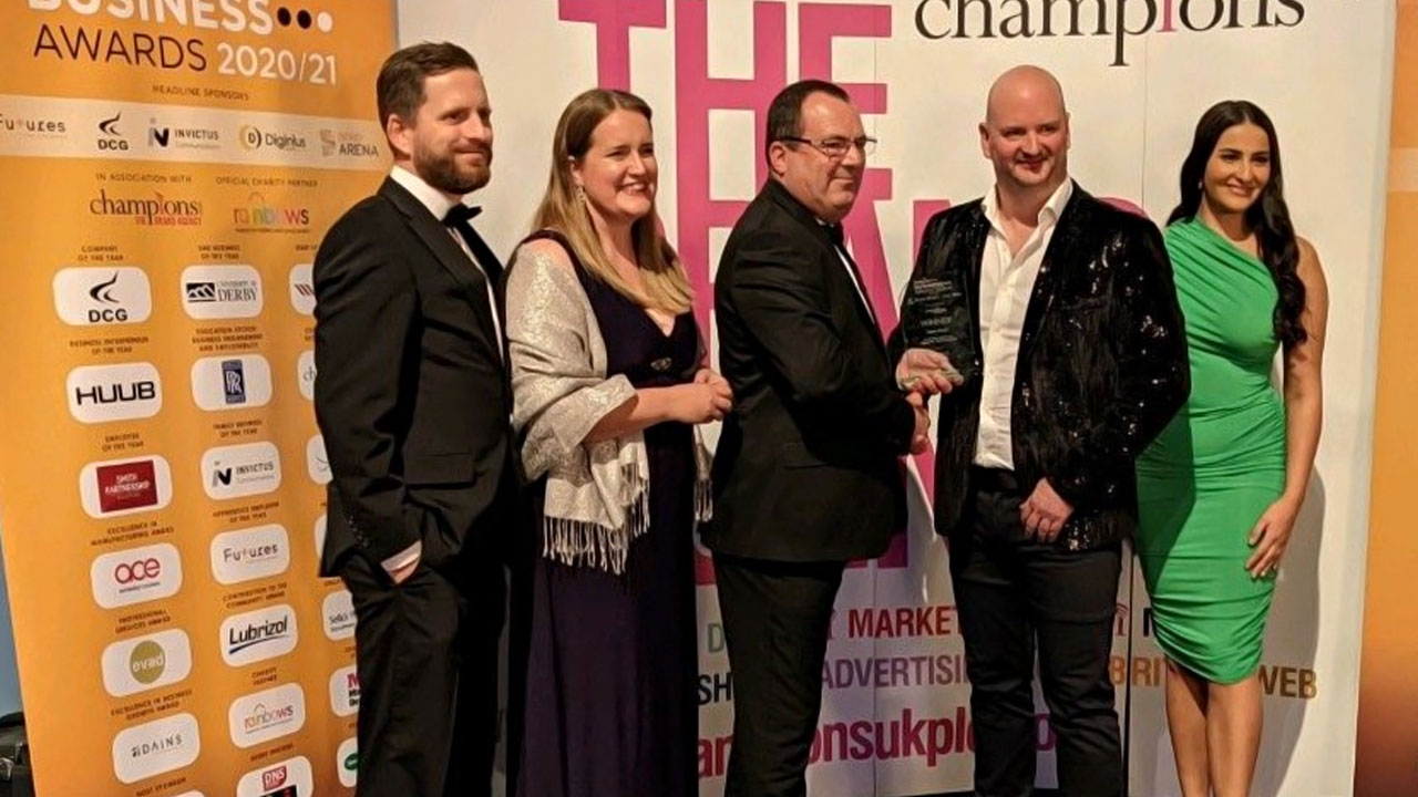 Group of people posing at a business awards ceremony with trophies and banners