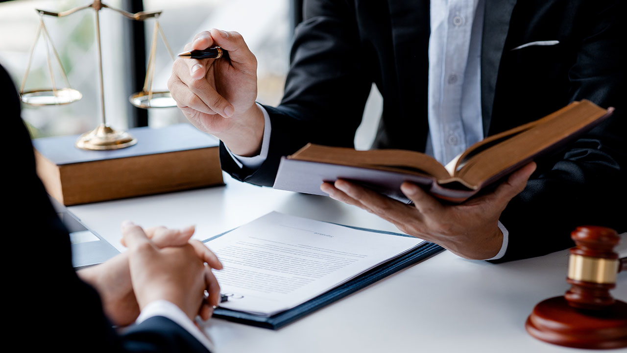 Two professionals in suits discussing legal documents with scales and gavel nearby