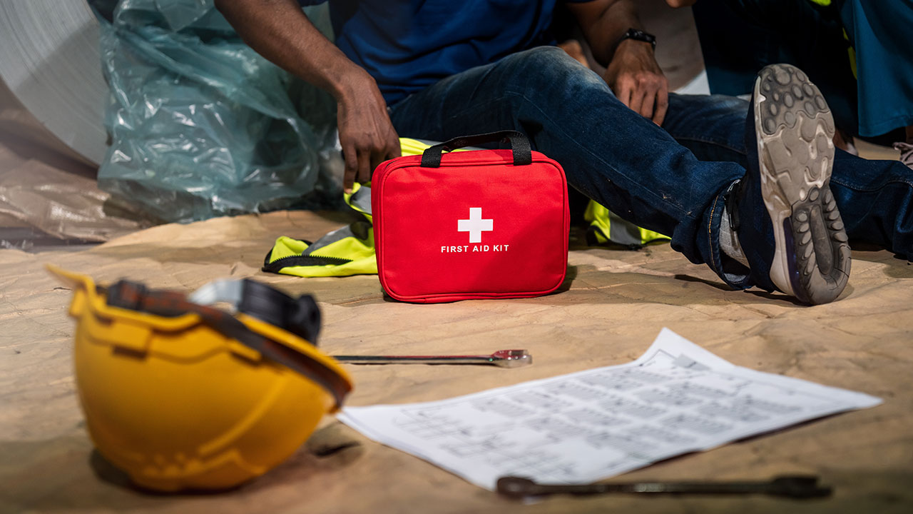 A red first aid kit sits beside a worker on the floor after a construction site accident
