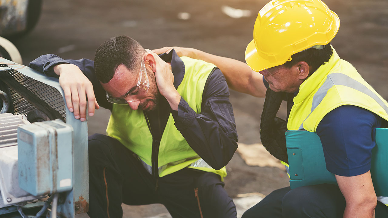 Worker comforting a colleague with an injury near industrial equipment