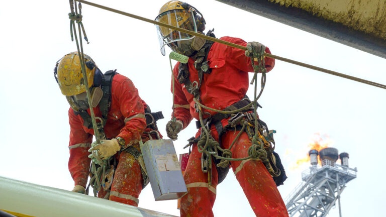 Rope access workers in red suits performing maintenance on industrial pipes