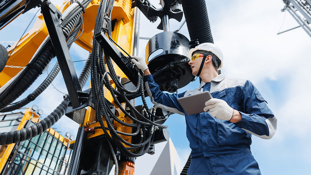 Technician inspecting heavy machinery outdoors while holding a tablet