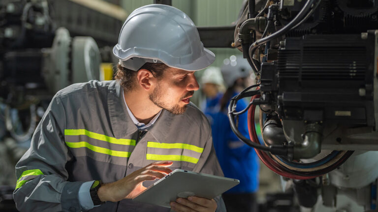 Worker inspecting industrial machinery with a tablet in a factory