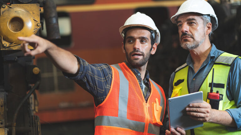 Construction worker pointing while colleague reviews plans on a tablet