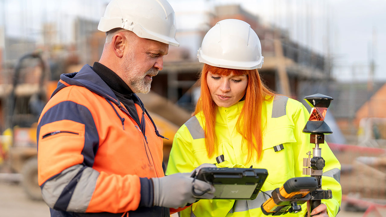 Engineers on construction site using a digital tablet beside surveying equipment