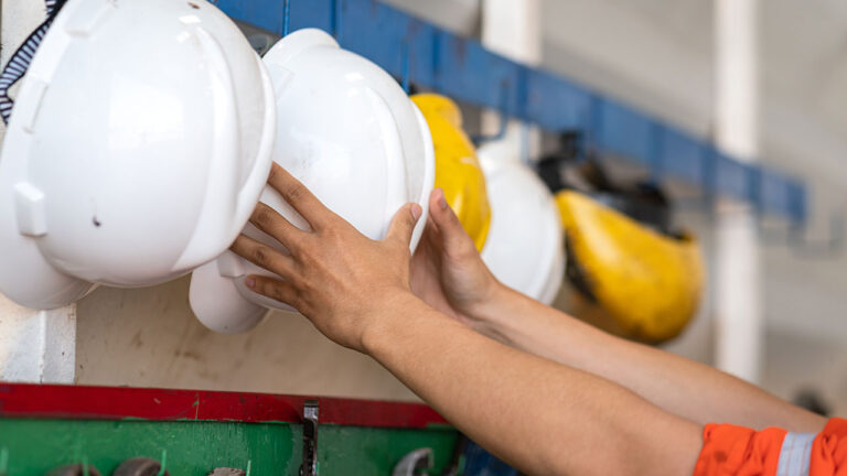 Worker reaching for a white hard hat on a rack in a site changing area