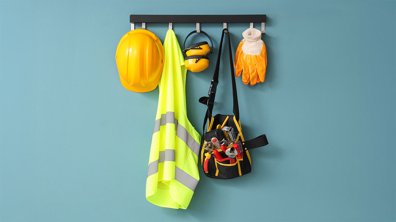 Safety gear including hard hat, high-visibility vest, gloves, and tool bag hanging on wall hooks