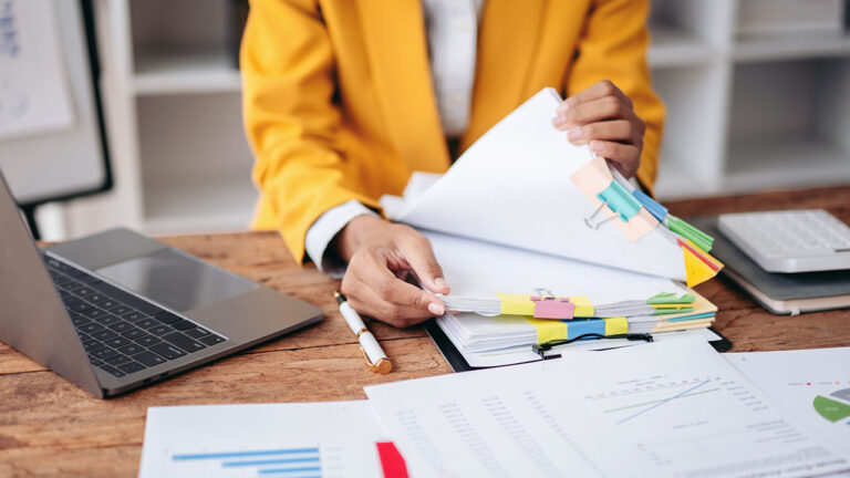 Person in yellow blazer organizing documents with charts and a laptop on a desk