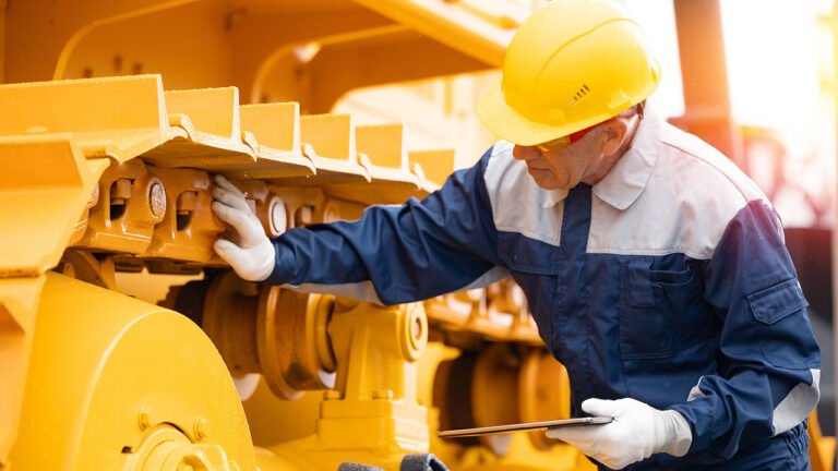 Technician inspecting large yellow machinery with a tablet