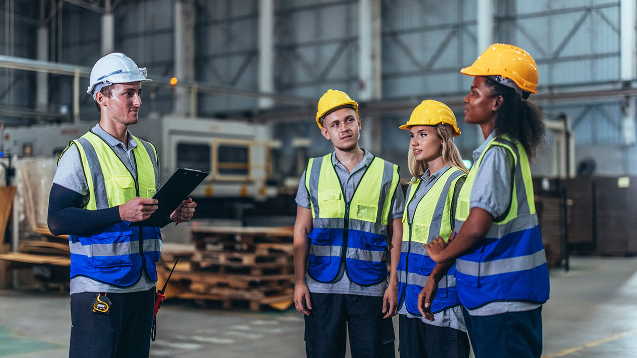 Group of construction workers listening to supervisor holding clipboard