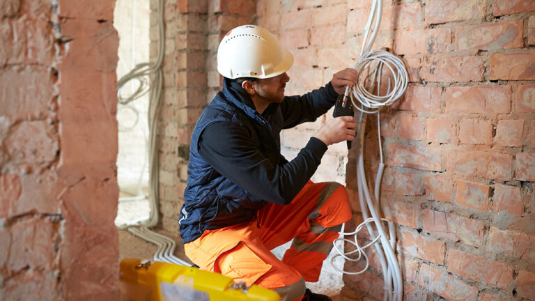 Electrician installing cables inside a brick wall during renovation