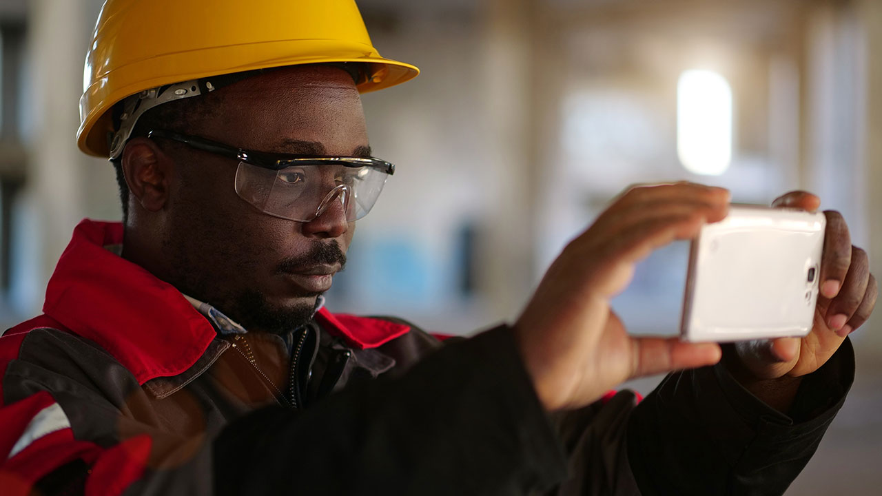Construction worker wearing safety gear taking a photo with a smartphone