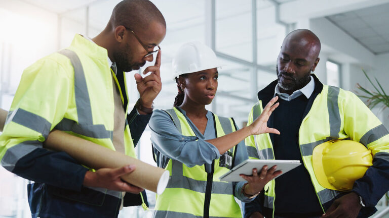 Team of engineers in safety vests discussing plans using a tablet