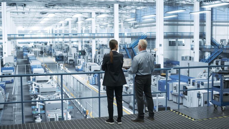 Two managers overseeing large manufacturing facility from balcony