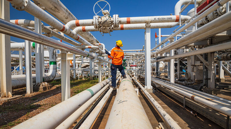 Worker inspecting industrial pipelines outdoors wearing safety gear