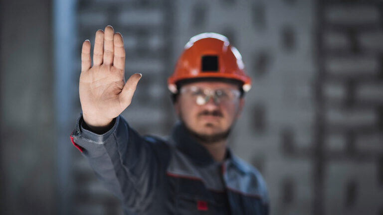 Construction worker raising hand to signal stop while wearing helmet and safety gear