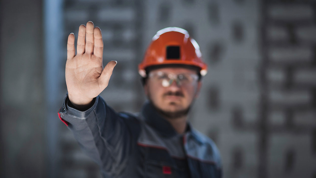 Construction worker raising hand to signal stop while wearing helmet and safety gear