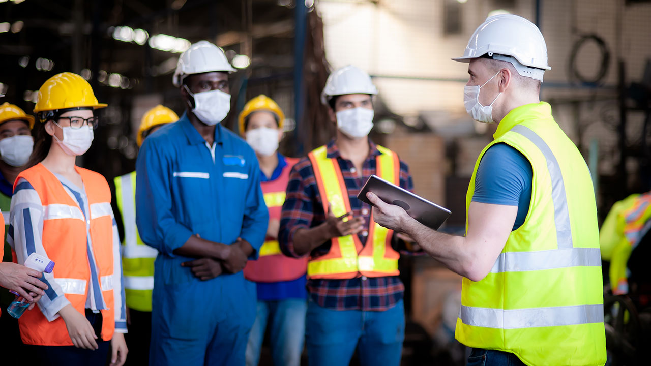 Construction supervisor addressing a group of workers wearing safety gear and masks