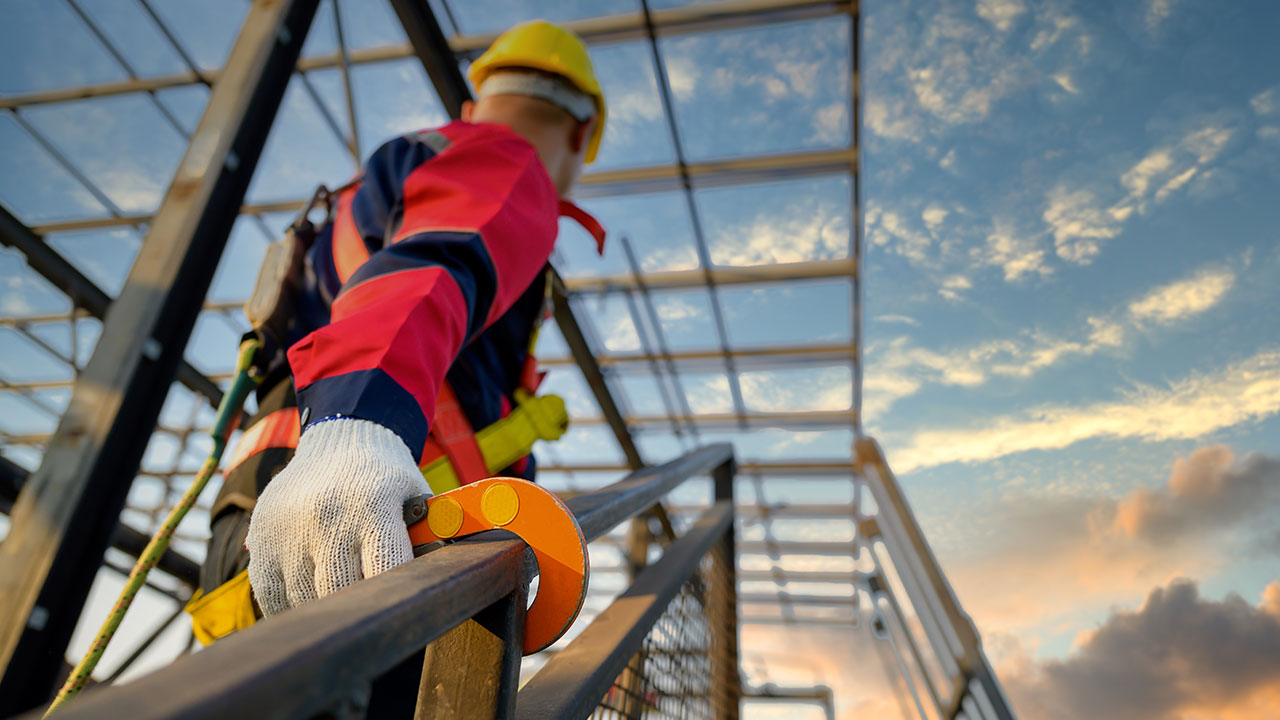 Worker in safety gear using fall protection on steel framework at sunset