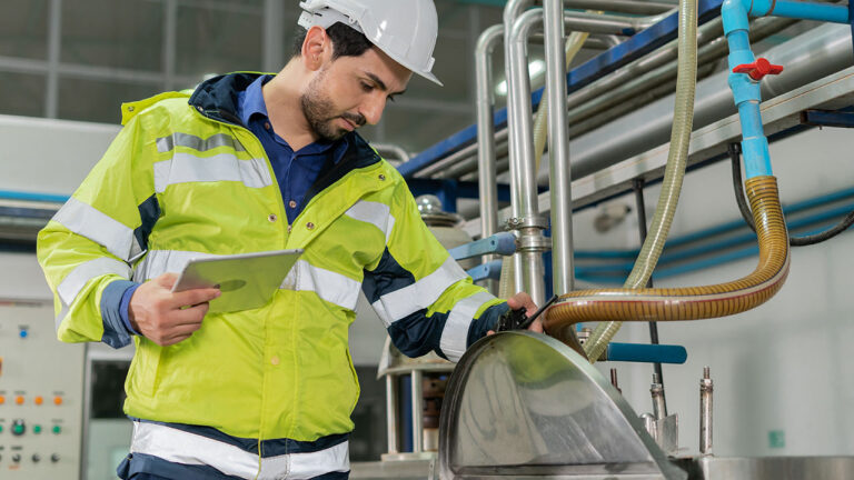 Engineer in reflective jacket and helmet inspecting equipment with tablet