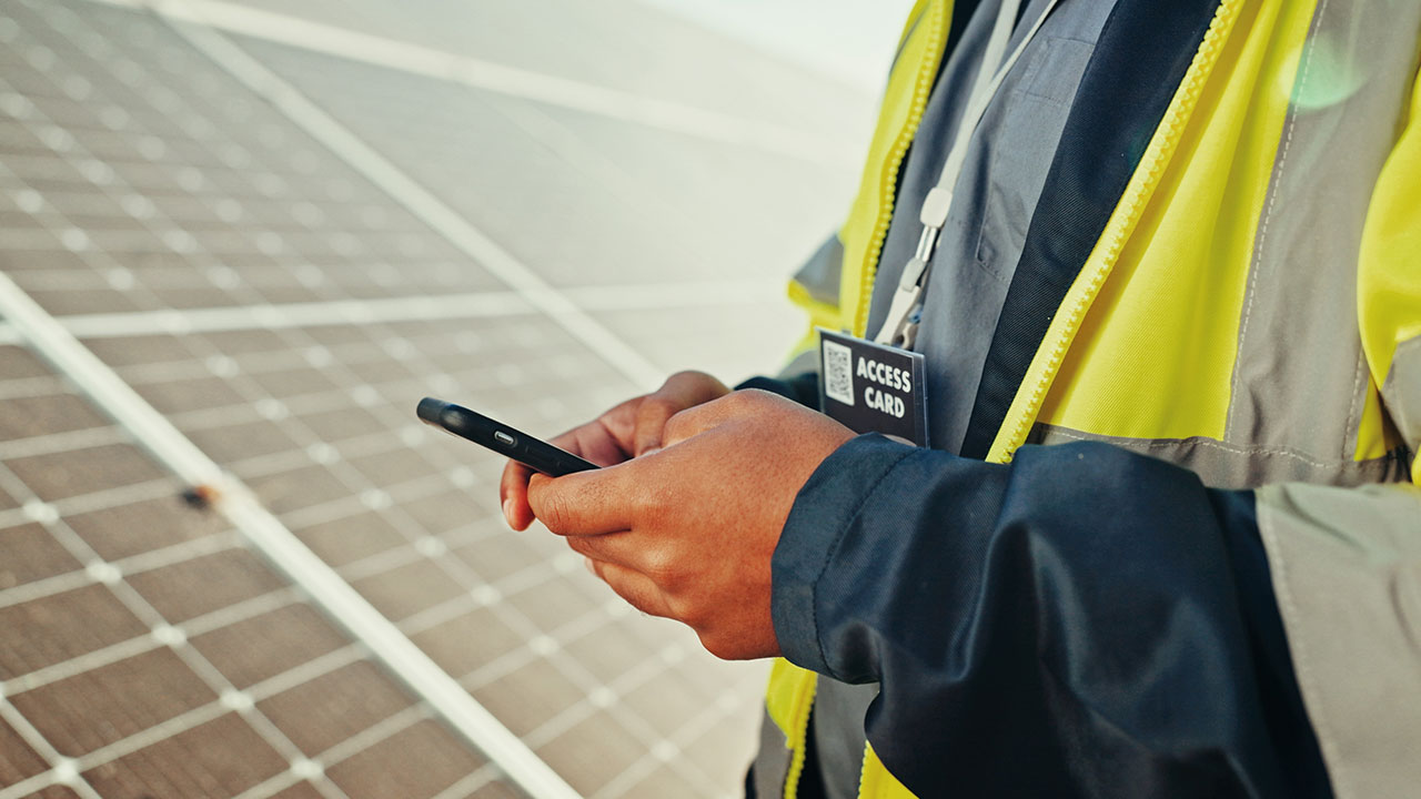 Worker in safety jacket using smartphone near solar panels