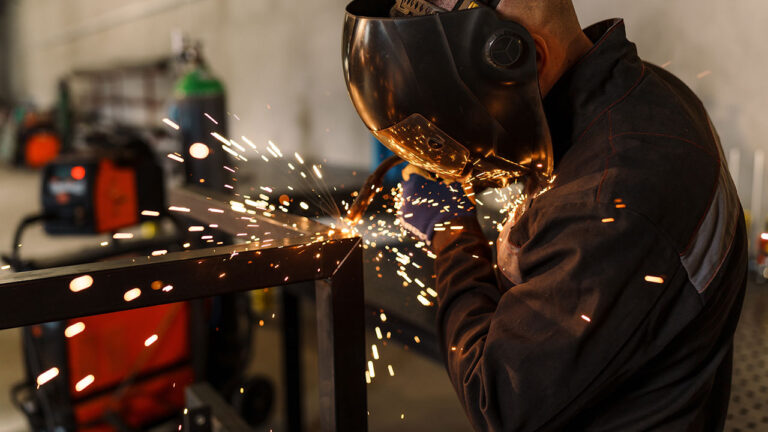Welder wearing protective gear working on metal with sparks flying