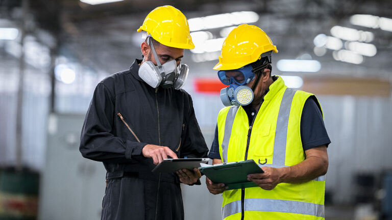 Two workers wearing respirators reviewing documents in a factory