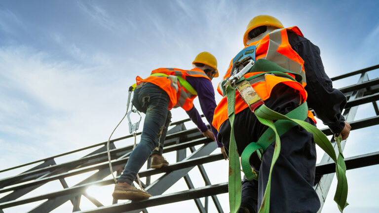 Construction workers in safety gear climbing metal framework