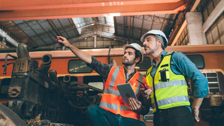 Two engineers inspecting machinery inside a large industrial workshop