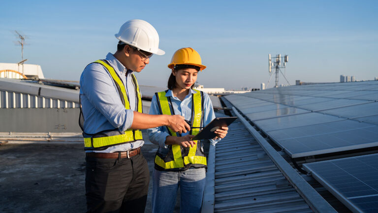 Engineers checking data on a tablet near rooftop solar panels
