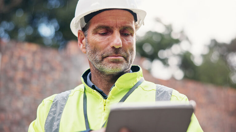Construction worker using a tablet outdoors while wearing a hard hat