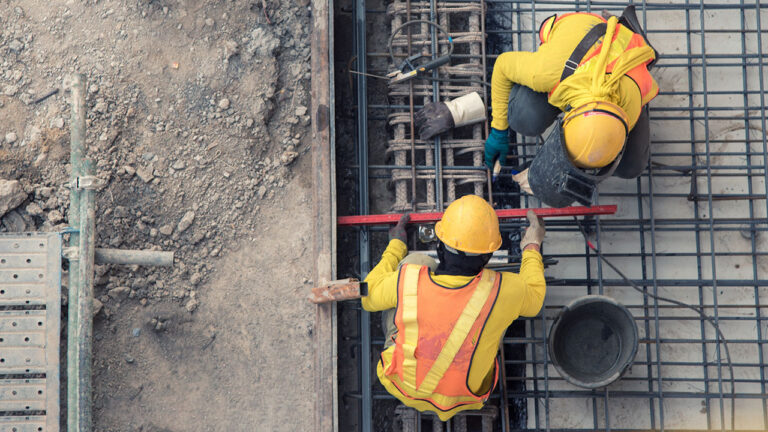 Two construction workers measuring steel reinforcement on a site