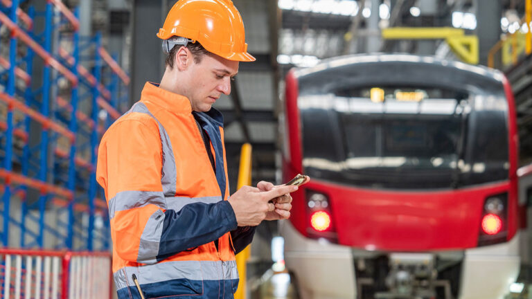 Rail worker using a smartphone near a train inside a maintenance depot