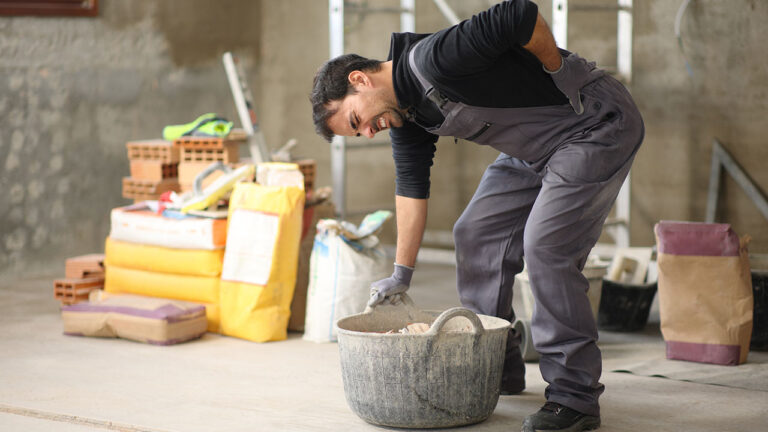 Worker lifting heavy bucket and straining back inside a construction area