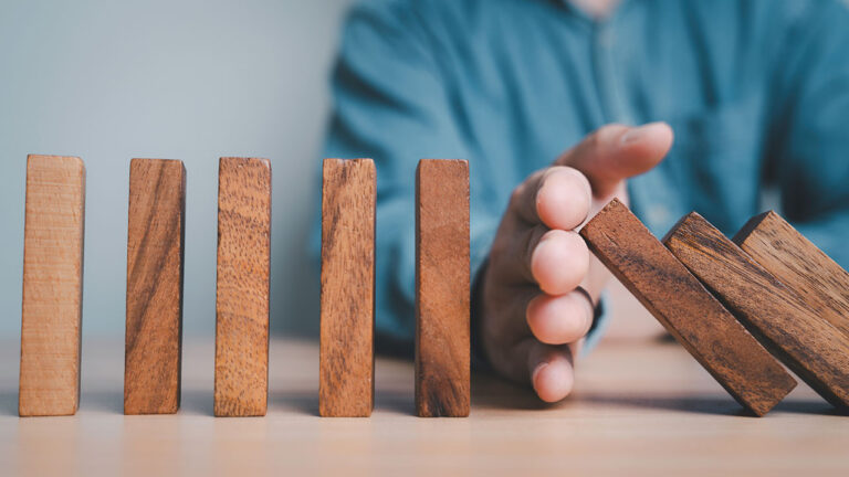 Hand stopping falling wooden blocks symbolising risk prevention or control