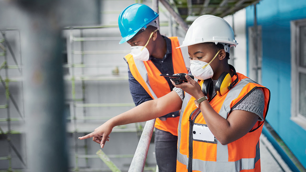 Two construction workers wearing masks and safety gear inspecting site