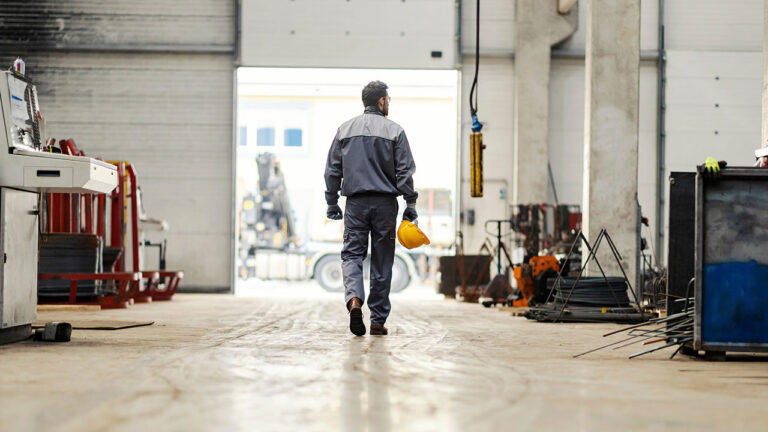 Worker walking through an industrial warehouse holding a yellow hard hat