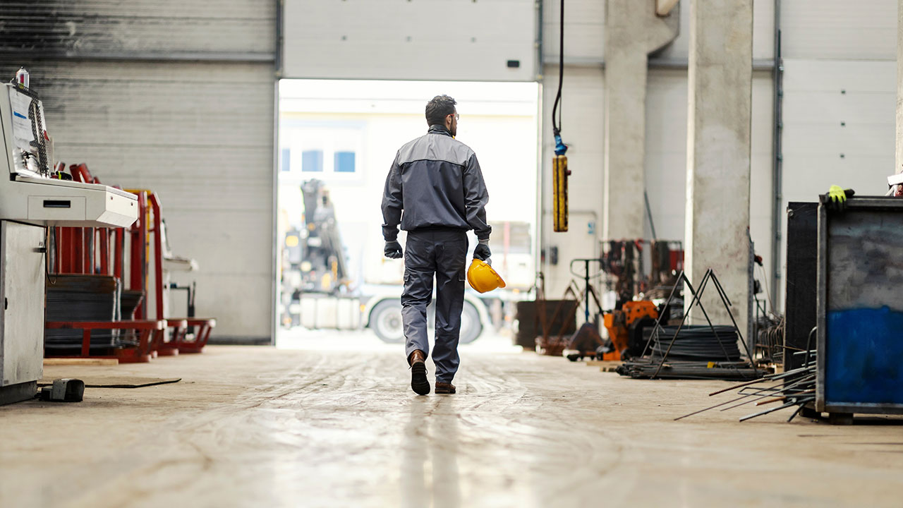Worker walking through an industrial warehouse holding a yellow hard hat