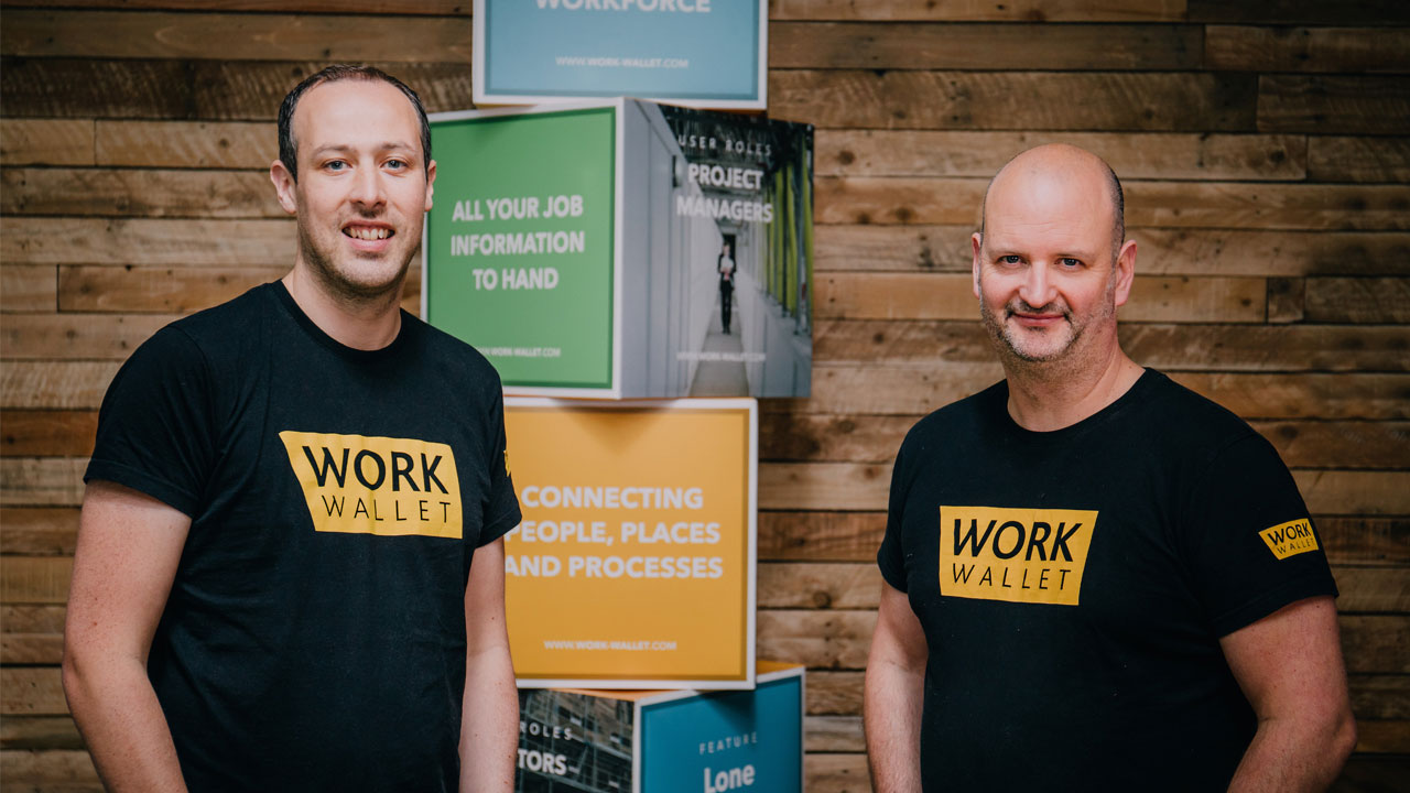 Adam and Jonny from Work Wallet pose in front of a marketing display