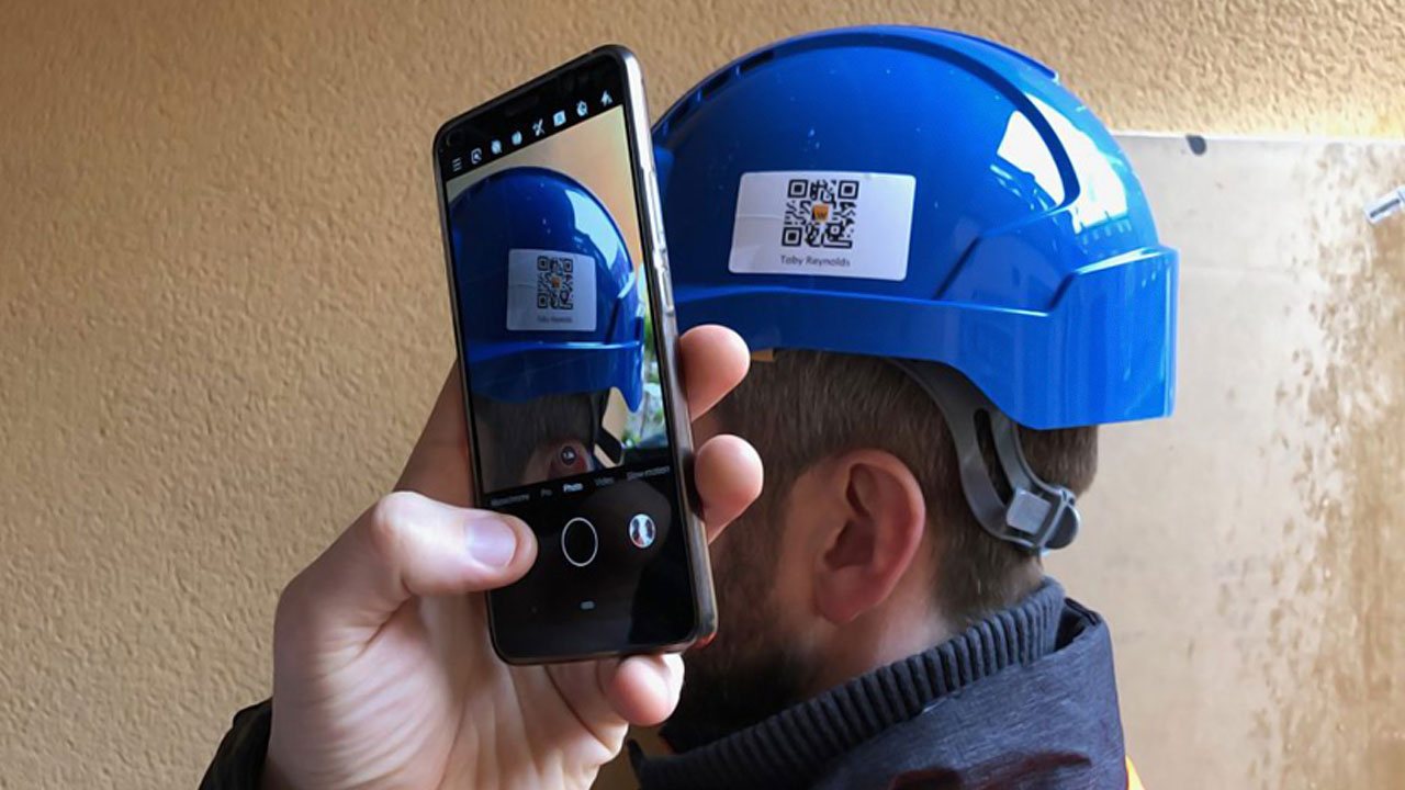 A person scans a QR code on a blue safety helmet using a smartphone