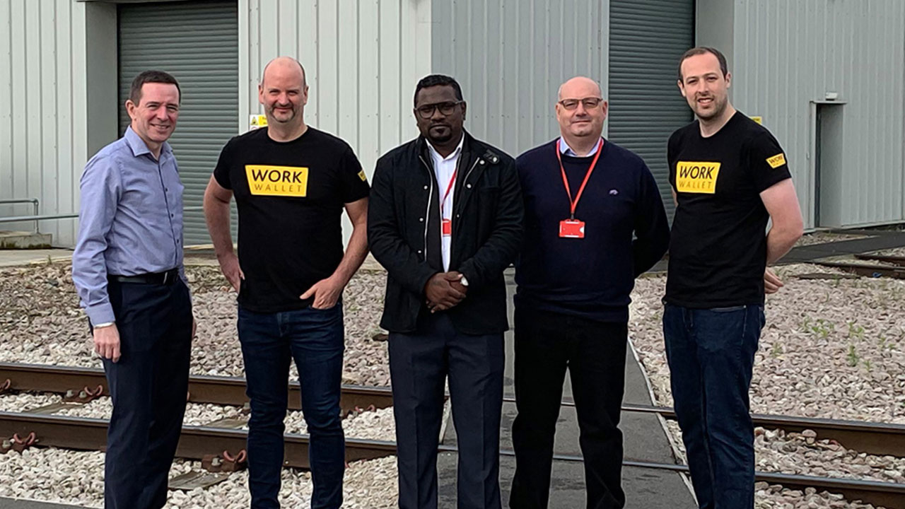 Five men stand together on a rail track outside an industrial building